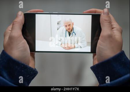 Online-Medizin. Der Patient spricht zu Hause per Videolink mit dem Arzt. Ein Mann gibt eine medizinische Fernberatung auf einem Smartphone. Eine Frau ist es Stockfoto