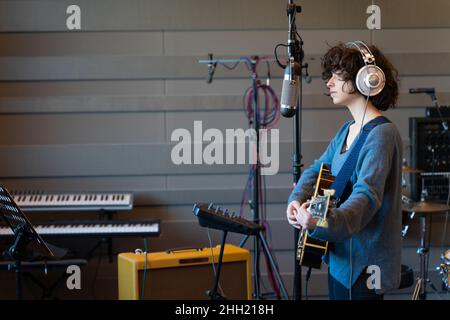 Eine junge Sängerin, die mit ihrer Gitarre einen Song in einem echt chaotischen Studio aufnahm Stockfoto