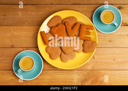 Hausgemachte Kekse in Form von Herzen und Buchstaben "LIEBE" und zwei Tassen Kaffee Espresso auf Holztisch. Draufsicht. Stockfoto