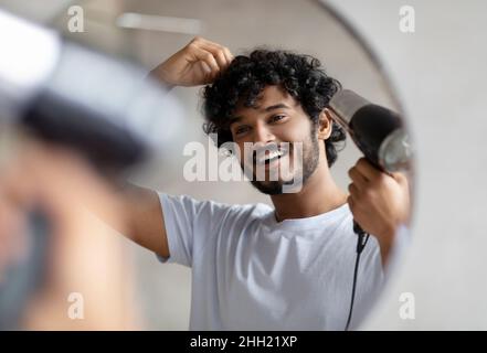 Aufgeregt indischen Mann mit Fön nach der Dusche, Trocknen seiner lockigen Haare, machen Frisur, morgendliche Routine Stockfoto