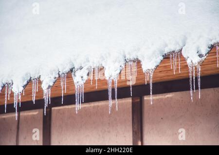 Scharfe, schöne Eiszapfen und geschmolzener Schnee hängen vom Dachüberhang. Eisschmelze im frühen Frühjahr. Stockfoto