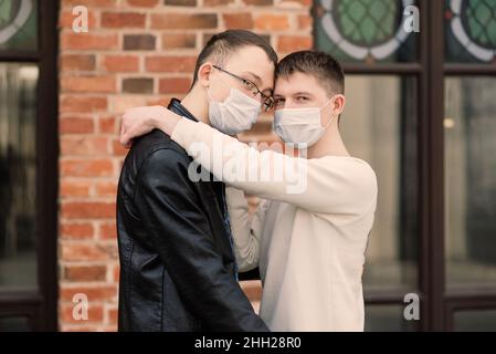 Junge schwule Paar trägt medizinische Maske, umarmt und küsst in der Stadt. Stockfoto
