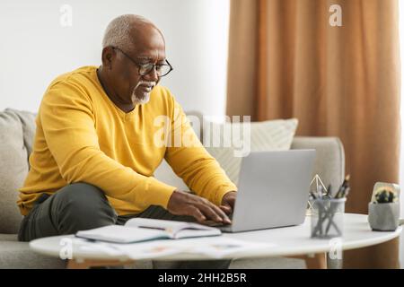 Senior Black Man Eingabe Auf Laptop Online Indoor Arbeiten Stockfoto