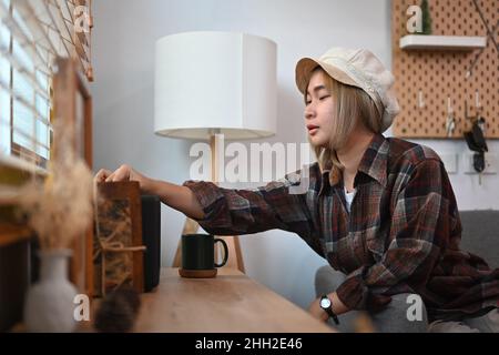 Lächelnde junge Frau, die im Wohnzimmer den kabellosen Lautsprecher anmacht. Stockfoto