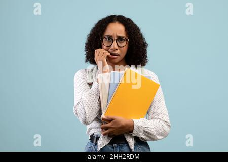 Beunruhigte afroamerikanische Studentin mit Notizbüchern und Rucksack, die in Panik Nägel beißen, besorgt vor dem College-Examen Stockfoto