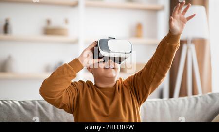 Fröhlicher Teenager, der VR-Brille verwendet und etwas Unsichtbares berührt Stockfoto