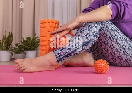 Das Mädchen sitzt auf dem Boden und massiert sich mit einem stacheligen Ball, um sich zu entspannen und zu zirkulieren Stockfoto