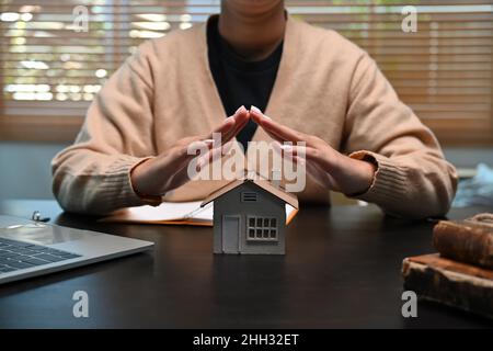 Frau Hände schützen kleines Haus Modell. Versicherungsimmobilienkonzept. Stockfoto