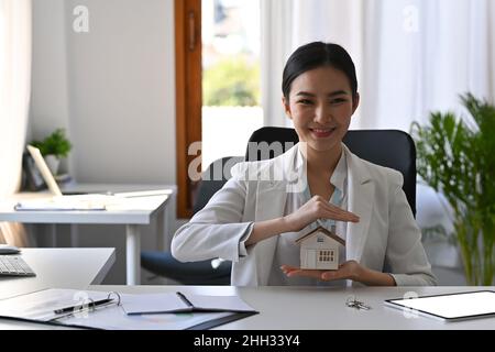 Schöne asiatische Frau Hände schützen Haus Modell. Versicherungs- oder Darlehensimmobilienkonzept. Stockfoto