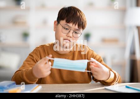 Gelangweilt asiatische teen junge halten schützende Gesichtsmaske Stockfoto