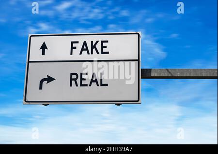 Straßenschild mit Wörtern gefälscht und real. Weiße zwei Straßenschilder mit Pfeil auf Metallmast auf blauem Himmel Hintergrund. Stockfoto