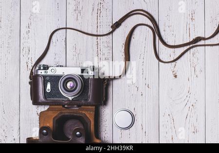 Eine alte Retro-Kamera in einer Ledertasche und eine Objektivkappe daneben. Vintage-Foto Stockfoto