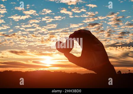 Silhouette der Hände hält Herzen auf Sonnenuntergang Himmel Hintergrund. Love Day Konzept Stockfoto