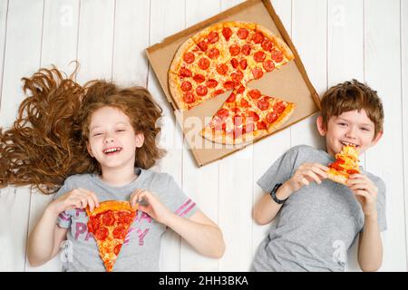 Kinder, die eine Pizza auf dem Holzboden halten. Quarantänefeier zu Hause. Stockfoto