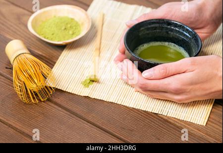 Mädchenhände halten Matcha-Tee in speziellen traditionellen japanischen Matcha-Teeschale mit Bambuslöffel und Schneebesen und Matcha-Teepulver Stockfoto