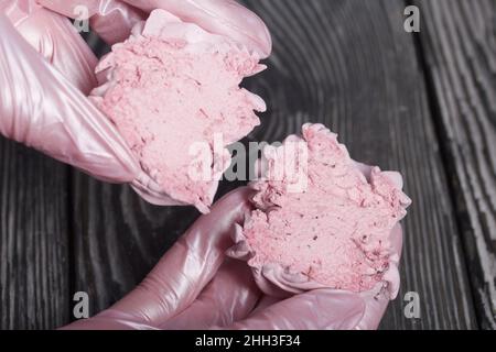 Eine Frau hält einen geschnittenen Marschmallow in ihren Händen. Vor dem Hintergrund von Kiefernbrettern. Nahaufnahme. Stockfoto