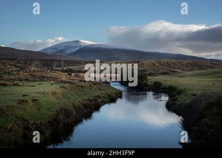 Ein Fluss am Rande des Wild Nephin National Park in Irland. Schnee auf den Bergspitzen der Wild Nephin Mountains. Stockfoto