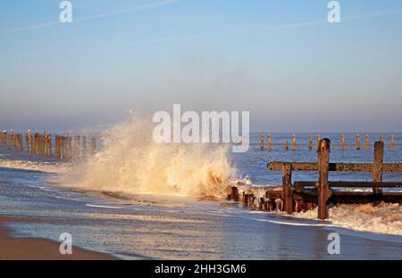 Eine Welle, die im Winter an der Nordnorfolk-Küste bei Cart Gap, Happisburgh, Norfolk, England, Großbritannien, gegen erodierte Meeresverteidigungen einstürzte. Stockfoto