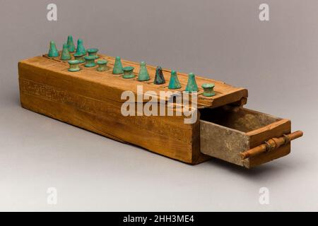 Spielbox mit Inschrift für Taia und seine Familie Ca. 1550–1295 v. Chr. Neues Königreich Diese Holzspielbox verfügt über zwei Spielflächen und eine Schublade zur Aufbewahrung von Spielsteinen und Wurfstäben, die als Zähler für die Bestimmung von Spielzügen in den Spielen verwendet wurden. Die obere Fläche ist mit zwanzig Quadraten für das Spiel tjau (Räuber) ausgelegt. Der Boden hat dreißig Quadrate für das Spiel senet (Passing). Im Neuen Königreich wurde Senet mit der Unterwelt in Verbindung gebracht; die Hindernisse des Spiels, die Gefahren entsprechen, trafen sich auf der Reise ins Jenseits. Im Grab von Nefertari, der Hauptfrau von Ramesses II, wird eine Szene dargestellt Stockfoto