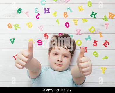 Kleiner Junge mit Regenbogen-Buchstaben, die Daumen nach oben zeigen. Schulkonzept. Stockfoto