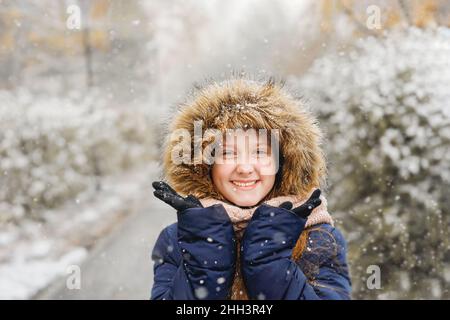 Nettes Mädchen fangen Schneeflocken Spaß im Freien in einem ersten Schnee. Stockfoto