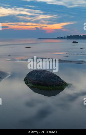 Blaue Stunde nach dem Sonnenuntergang über der felsigen Ostsee kosten. Kleine Steine und große Felsbrocken im Meer. Langzeitbelichtung Stockfoto