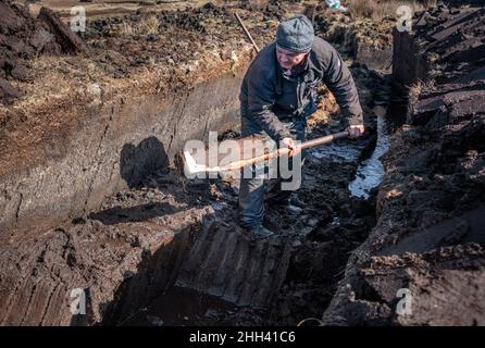 Ein irischer Rasenmäher, der mit einem Sleán Rasenflächen schneidet, die traditionelle Art des Rasenmähens, wie es seit Ewigkeiten gemacht wird. Stockfoto