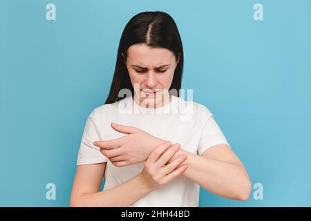 Porträt von müden jungen weiblichen Armen, die ihr schmerzhaftes Handgelenk halten, verursacht durch längere Arbeit, isoliert auf blauem Hintergrund. Karpaltunnelsyndrom, Arthritis Stockfoto