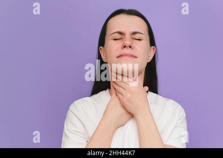 Nahaufnahme einer kranken jungen Frau, die an Halsschmerzen leidet, isoliert auf einer purpurnen Studiowand. Ursachen von Rachenschmerzen sind Grippe, Erkältung, bakterielle in Stockfoto