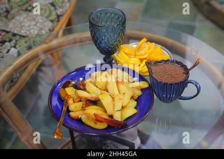 Gebratene Kartoffeln, geschnittene Zitronen und Gläser auf einem Glastisch Stockfoto