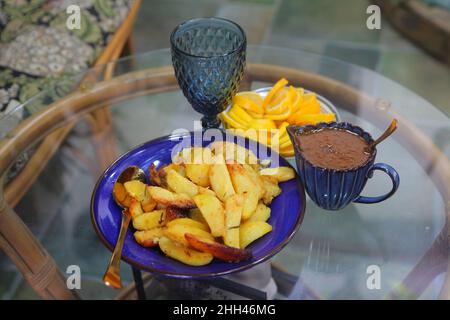 Gebratene Kartoffeln, geschnittene Zitronen und Gläser auf einem Glastisch Stockfoto