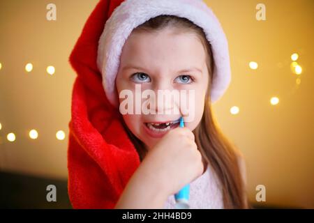 Kleines Mädchen, das sich die Zähne in einem Weihnachtshut putzt Stockfoto