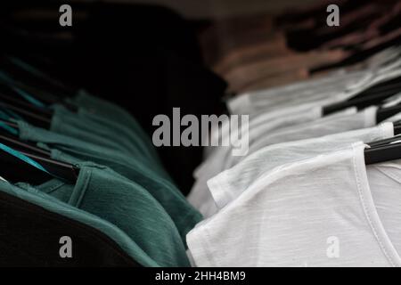 Einige benutzten Kleidung, die auf einem Flohmarkt auf einem Regal hing. Hintergrund des Kleides. Selektiver Fokus. Stockfoto