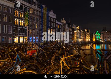 AMSTERDAM - 14. DEZEMBER 2019: Berühmte tanzende Kanalhäuser am Damrak-Kanal bei Nacht mit vielen Fahrrädern vorne Stockfoto