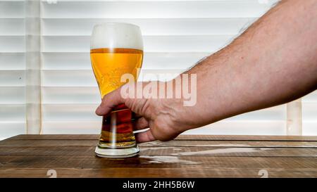 Mans Hand nimmt Bier in Glas auf Holztisch Stockfoto