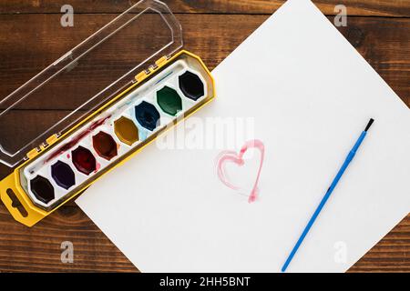 Bemalte Herzen auf Papier von oben auf Holztisch Stockfoto