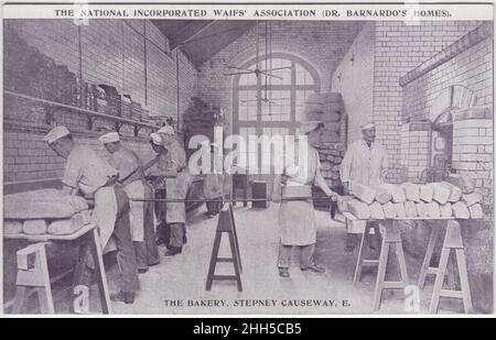 Die National Incorporated Waifs' Association (Dr. Barnardo's Homes), The Bakery, Stepney Causeway, London, E. Boys bei der Arbeit in der Bäckerei, die vom Bäcker beaufsichtigt werden. Gebackene Brote werden aufgeschichtet und Brotdosen befinden sich auf Regalen entlang der Wände Stockfoto