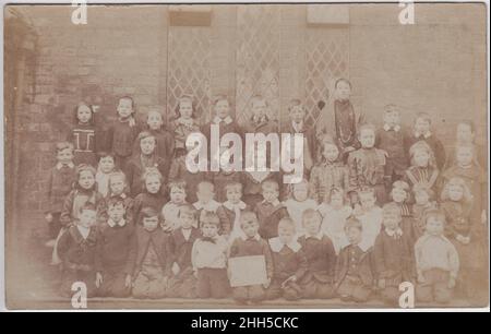 Schulfoto mit Kindern unterschiedlichen Alters, alle unterschiedlich gekleidet. Foto aus dem frühen 20th. Jahrhundert Stockfoto