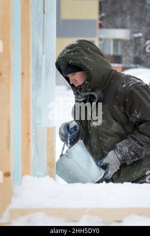 Ein Eisstädter in einer grünen Kapuzenjacke gießt Wasser aus einem Eimer über einen Eisblock Stockfoto