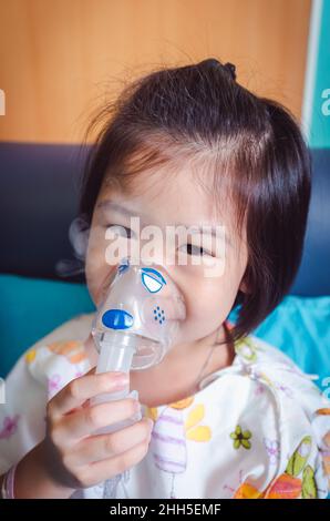 Glückliches asiatisches Kind hält einen Maskendampf-Inhalator für die Behandlung von Asthma. Atmung durch einen Dampfvernebler.Krankheit Mädchen im Krankenhaus eingeliefert. Stockfoto