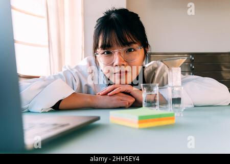 Junge Chemikerin mit Brillen, die im Labor auf den Tisch gelehnt sind Stockfoto
