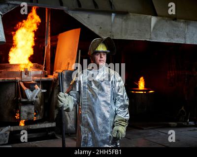 Kontemplativer Arbeiter mit blauem Kragen, der Helm und Schutzanzug in der Metallindustrie trägt Stockfoto