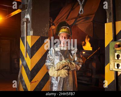 Lächelnder Metallarbeiter mit Arbeitsschutzkleidung in Stahlwerk Stockfoto