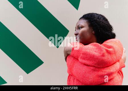 Plus Size Frau trägt roten Pullover umarmt sich selbst. Stockfoto