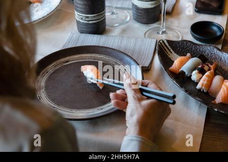 Frau hält Sushi mit Essstäbchen im Restaurant Stockfoto
