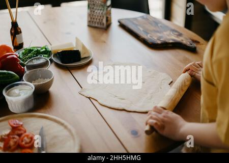 Junge bereitet Pizzateig mit Nudelholz auf dem Tisch zu Stockfoto