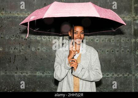 Teenagermädchen mit Regenschirm, der vor einer schwarzen Wand steht Stockfoto