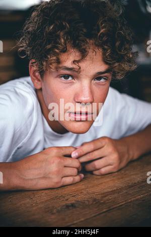 Teenager mit lockigen braunen Haaren, die auf den Tisch gelehnt sind Stockfoto