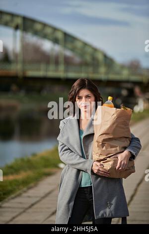 Frau, die Lebensmittel in einer Papiertüte auf dem Fußweg trägt Stockfoto