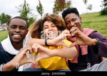 Glückliche Freunde, die mit den Händen im Park Herzform Formen Stockfoto